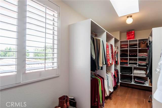 Walk-in closet has wood floors, skylight and organized custom clothes wardrobes, window and skylight.