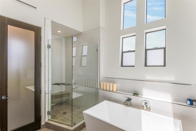 Primary suite bath with frameless shower, soaking tub, natural light and separate water closet