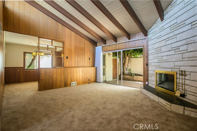 Through the front door there is an entry foyer with a doorway on the left to a large sunken master bedroom and bath. The hallway then opens into the large living room. The dining room and kitchen are to the left, separated by a wooden divider display case. There is a full wall length floor to ceiling stone faced fireplace with a slate hearth and there is a slider leading to the rear patio yard area. The room is spacious with vaulted beamed ceilings.