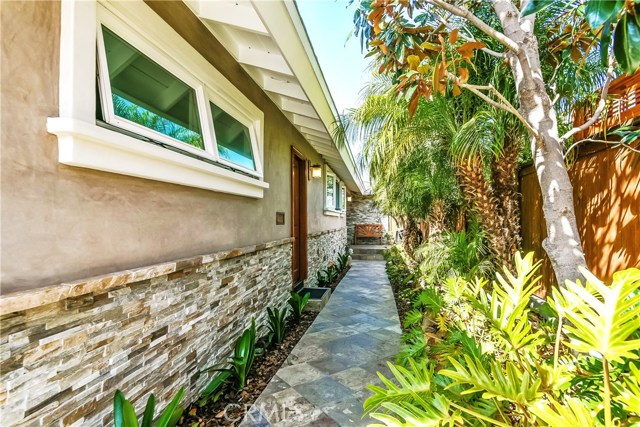 The stone pathway leads to the entrance of the house through the lush landscaping where the walls of the home are attractively finished in stacked ledger stone accents.