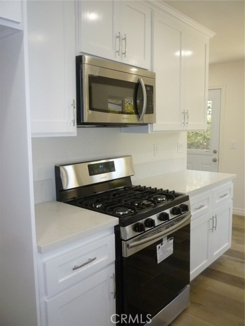 New stainless steel stove and microwave oven/hood. White shaker style cabinets and white quartz countertops.