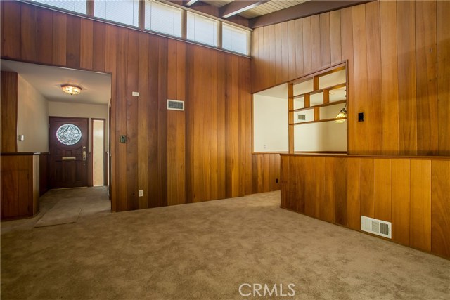 This is another view from the living room back towards the front entry door and foyer. The sunken master bedroom is towards the front entry through a doorway on the right and the dining room and kitchen are towards the right past the room divider. The slopped beamed ceilings are fronted by upper clerestory windows which flood the rooms with light in classic 1950's style..