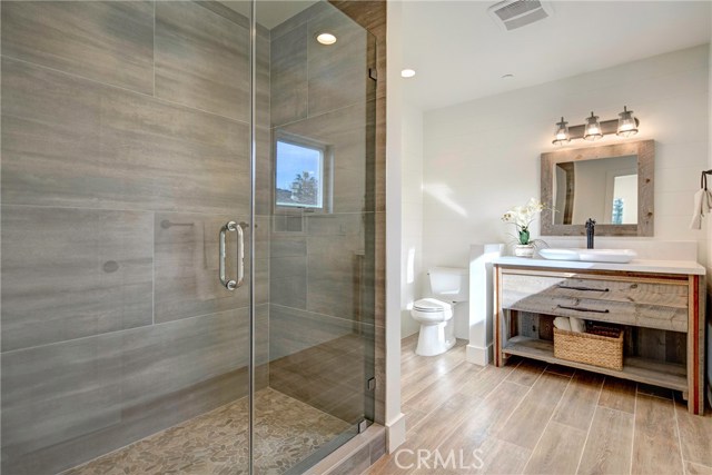 Downstairs suite - walk-in shower with porcelain wall tiles, rain shower head, pebble shower floor, reclaimed wood vanity, Quartz countertop, shiplap walls, and wood-like porcelain tile flooring.