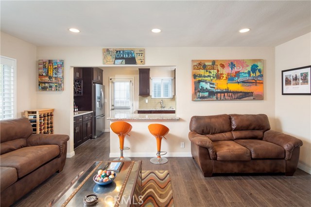 The living room is a bright an open space with wood-style floors, recessed lighting, and plantation shutters.