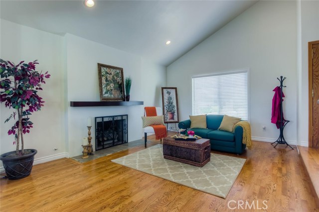 The warm and inviting living room also boasts vaulted ceilings with recessed lights, wood floors and a lovely fireplace with wood mantle.