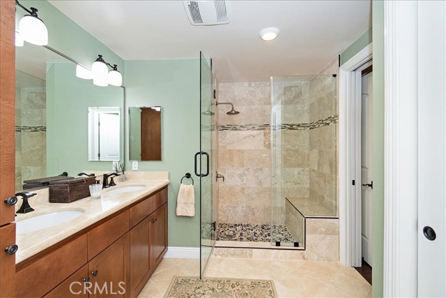 Master walk in shower features travertine tile and frameless doors
