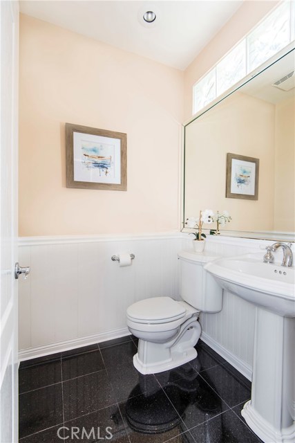 Powder room on 1st floor, adjacent to family room, with wainscoting, granite floors and natural light filtering in.