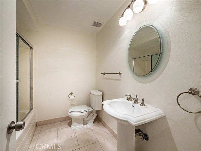 Second bathroom with tub/shower with glass doors, pedestal sink and tile floors.