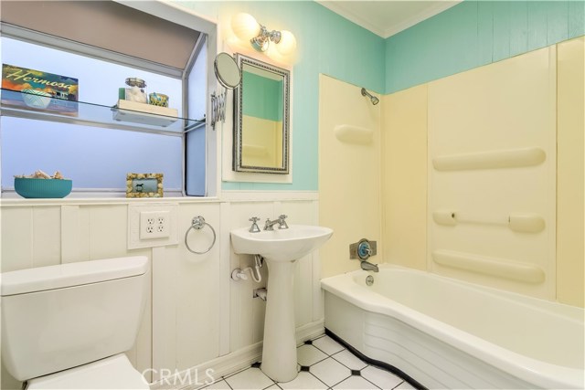 The lower level full bath has a vintage feel with a pedistal sink, tub, wainscotting, tile floors and a large garden window