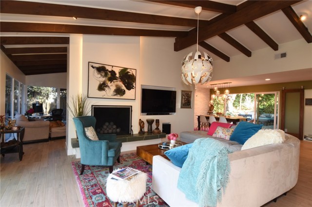 Living room is so inviting with gorgeous flooring, beamed ceilings, pretty fireplace with hearth, and built in TV nook!