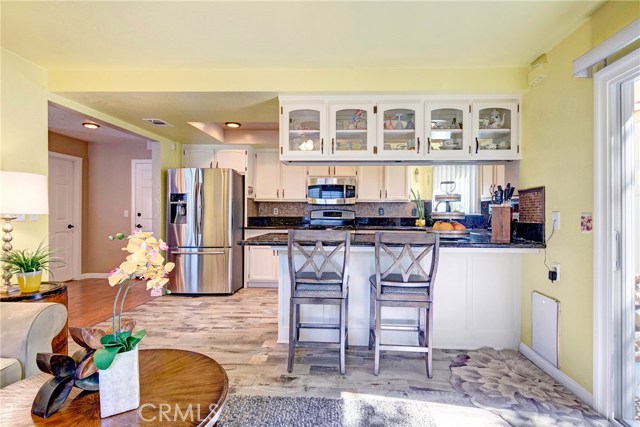 Sunny, light-filled kitchen with breakfast bar, beautiful tile backsplash, tons of cabinet storage, stainless appliances, granite counters, recessed lighting, adjacent family room, and backyard access.