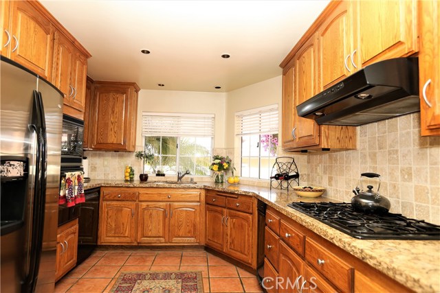 Kitchen with built-in range, micro, dishwasher, 5-burner gas cooktop with exhaust hood, and trash compactor.  Cabinets are refinished oak with contemporary pulls.  Granite countertops with tumbled travertine stone backsplash.  Recessed lighting.  Tile floor.