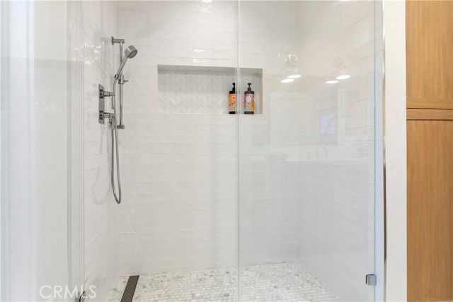 The primary bedroom - Phylrich shower head, shower rail, temperature valve and overhead rainhead in polished chrome. Linear drain system in shower. Field Tile in White from Mission Tile West on shower walls
Chevron Glass Tile by Artistic Tile, Swingin’ Chevron Be Bop White Glass Mosaic on niche
Calacatta Gold Broken Joint Mosaic polished stone by Artistic Tile on shower floors.
