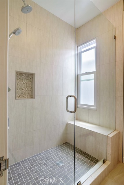 Renovated porcelain tile shower with two shower heads, shower seat and window with privacy glass for airflow and sunlight.