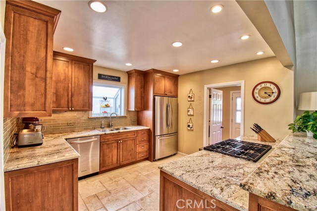 Cherry Cabinets, glass back splash & travertine stone floors grace the kitchen & laundry room beyond