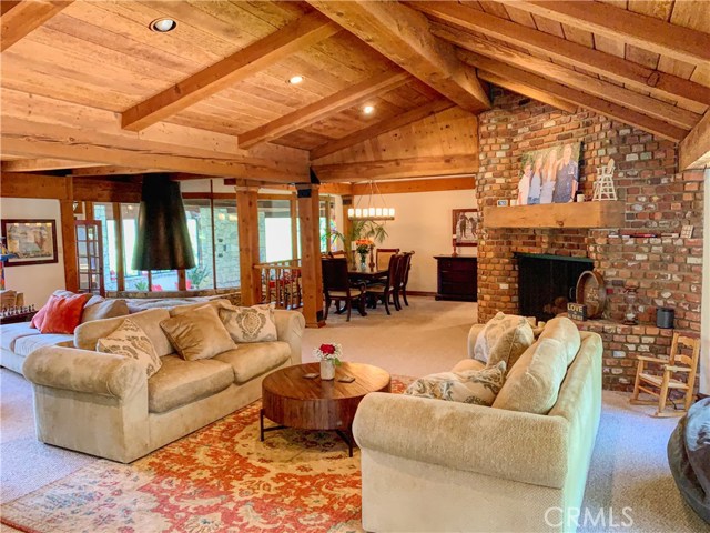 View of the living room and fireplace that begins to characterize the open flow of this home. Beautiful wood beamed ceilings adding warmth and coziness throughout.