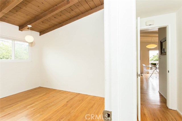 3rd bedroom with natural wood floors and wood beam ceiling. Split view into hallway and living area.