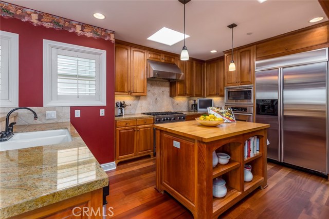 Cook's kitchen with butcher block style island, 6 burner Viking range, double ovens, stainless appliances, granite counter tops, and skylights.