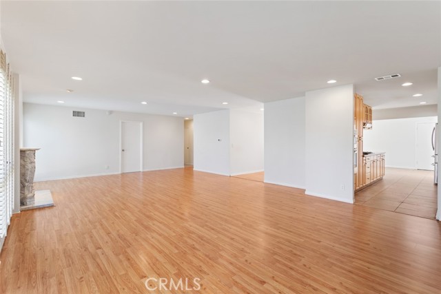 Spacious living room with a fireplace and kitchen shown to the right; recessed lighting throughout.  Floor length plantation shutters.