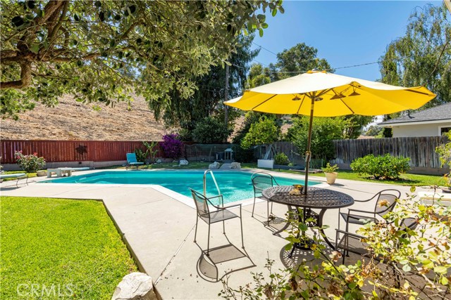 Beautifully maintained backyard features grassy areas, pool, space for lounging and eating, and rolling hills in background