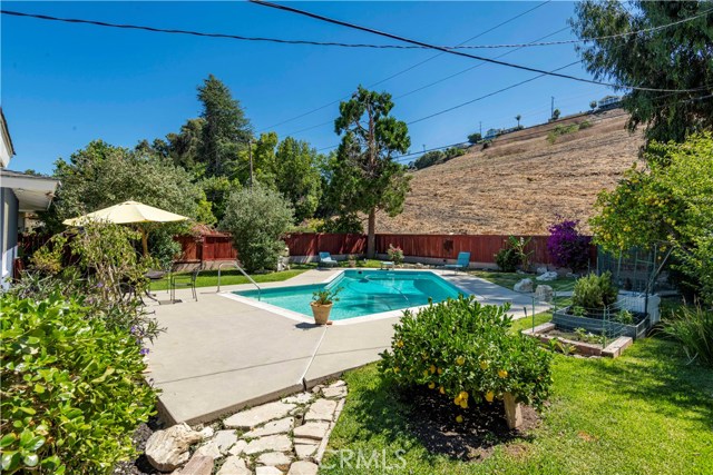 Beautifully maintained backyard features grassy areas, pool, space for lounging and eating, and rolling hills in background