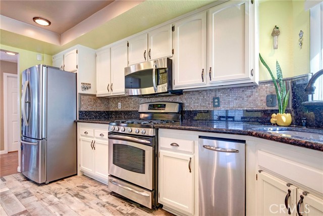 Sunny, light-filled kitchen with breakfast bar, beautiful tile backsplash, tons of cabinet storage, stainless appliances, granite counters, recessed lighting, adjacent family room, and backyard access.