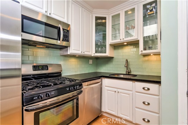 The kitchen backsplash wall is finished in green glass tile, the countertops are black quartz stone, there are glass display cabinets and the under counter lighting brightens up the work areas and creates a nice accent