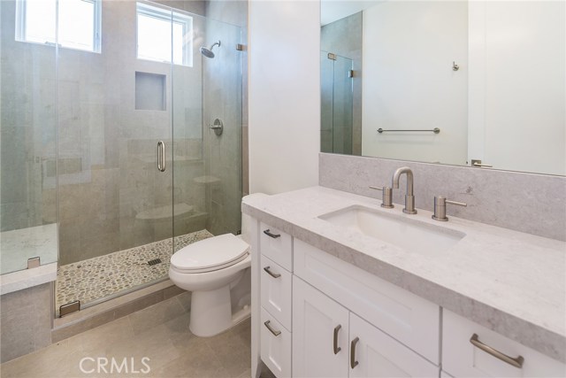 Hallway bathroom has pebble bottom shower stall with frameless glass enclosure and beautiful vanity with quartz counter.