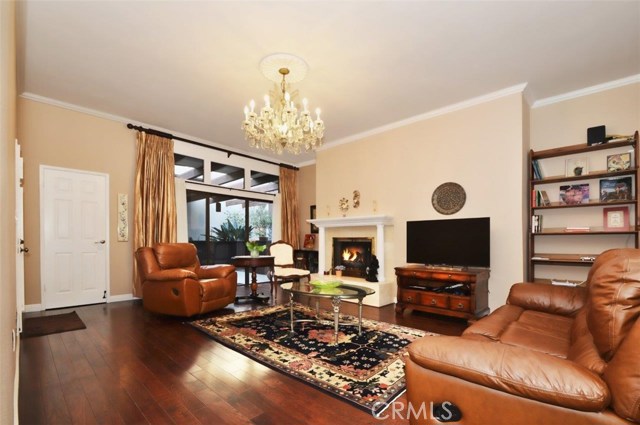 View of the spacious living room with fireplace, warm wood floors, crown molding, and elegant chandelier. Your front patio lies beyond the sliding glass door. This front patio is one of TWO patios at this fabulous property.