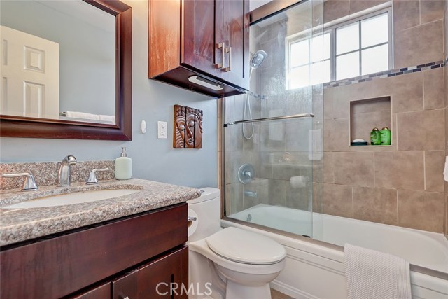 Upgraded bathroom with granite countertop, tile shower with insets and glass shower door.