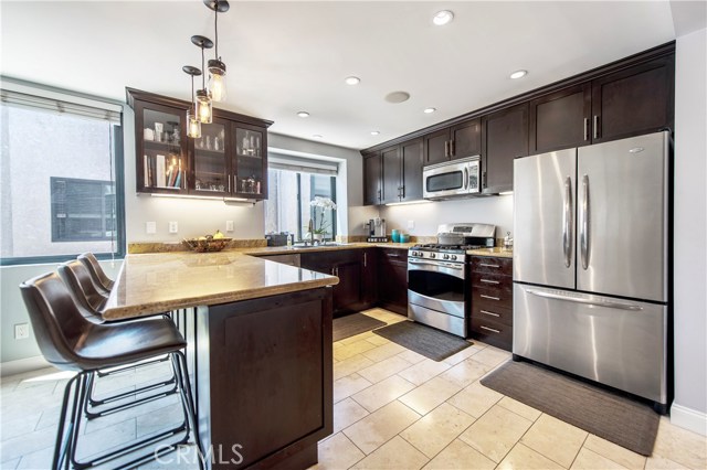 Beautifully remodeled kitchen with breakfast bar, rich espresso cabinetry, stainless appliances, custom lighting, travertine floors and granite countertops