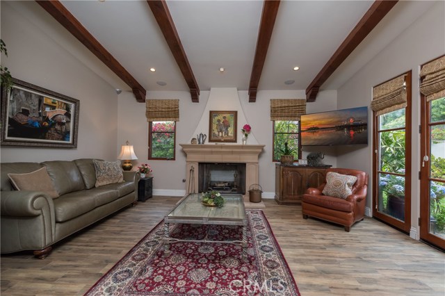 Welcome to the awesome family room with beamed ceilings, wood-like tile floors, beautiful fireplace, and French doors that lead to the lushly landscaped rear yard with patio w/BBQ area, wrap-around grassy yard, and pool and spa!