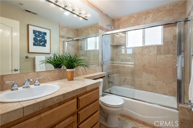 Bathroom #2 - Servicing the 2 bedrooms on the entry level, it features a shower and tub enclosure, warm travertine tile finishes, ample counter space and natural wood cabinetry.
