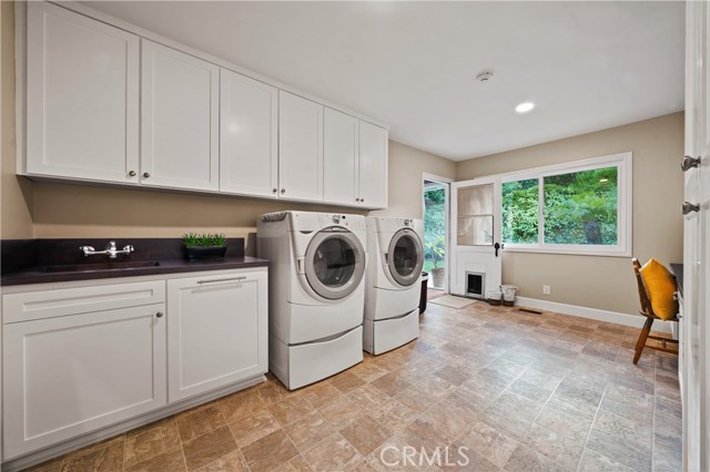 Large and spacious laundry room that features custom hand stained butcher block countertops, stainless tub sink desk and workspace, vast amount of storage and separate cleaning closet.
