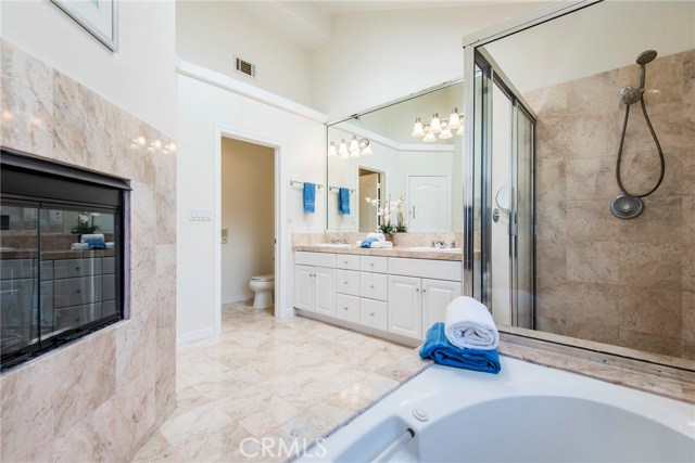 Gorgeous natural colored marble lines the master bathroom.  Note the dual vanities, separate toilet room, spa tub facing fireplace, and spacious shower.