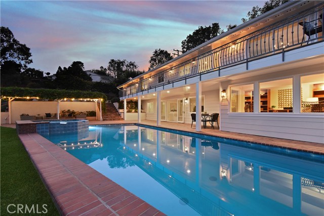 Twilight view of covered patio with string lights, pool, jacuzzi and balcony
