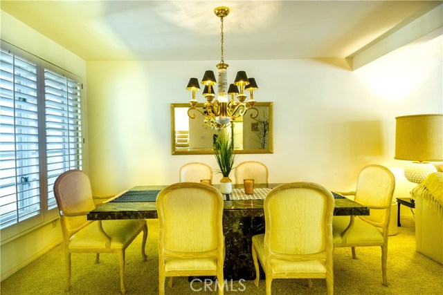 Formal dining room with brass chandeliere, windows with plantation blinds. Open flow into living room.