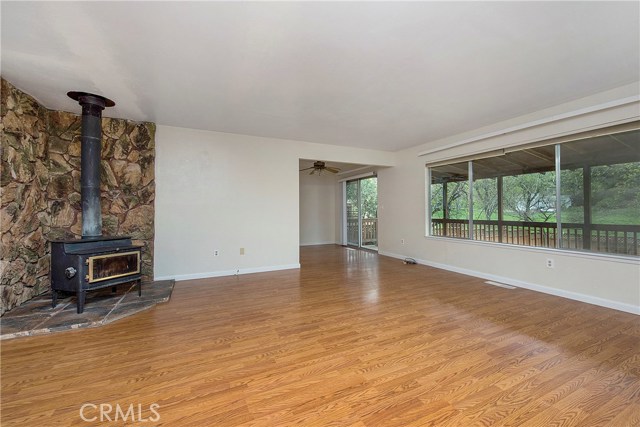 Large living room with laminate flooring, wood-burning fireplace with rock surround, and picture windows