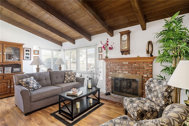 Very nice living room has heavy wood beam ceilings, brick fireplace, wood laminate flooring, sunny corner windows and dining area to left of this picture.