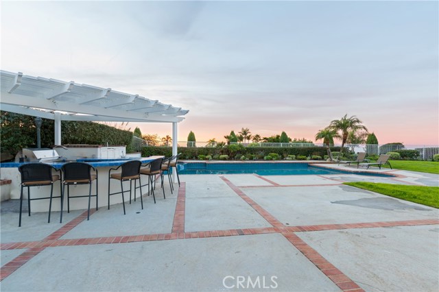 View of the outdoor kitchen seating area with pool and grass beyond.  This home seems to have everything!!