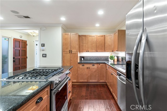 The gorgeous kitchen is upgraded with custom cabinetry, dark granite countertops and peninsula, newer stainless steel range cooktop, and stainless steel refrigerator and dishwasher.