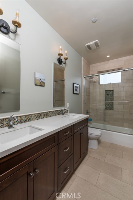 Upstairs hall bathroom has double sinks, quartz counters, and nice tile flooring.