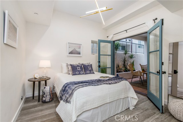 Sunny and bright guest bedroom with Italian wood-look porcelain tile and French doors leading to an outdoor patio.