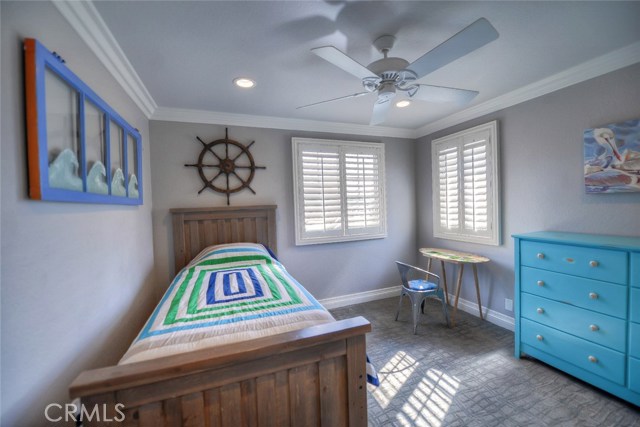 Second upstairs bedroom with ceiling fan, plantation shutters, crown molding, and closet organizers.