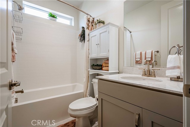 Second primary en-suite bathroom features quartz vanity with stainless steel hardware, mirror, toilet and tub/shower with a small window to allow natural light in.