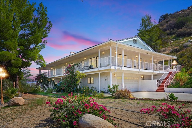 18345 Sanders Drive Lake Elsinore, California Welcome home to the most fantastically unique home in Lake Ridge. Tucked away on a quiet and secluded street, this 5 bed 3.5 bath two-story home provides the trifecta: serenity on a wrap-around porch, fantastic view of the hills, and a relaxing view of the lake. The home sits on 1.31 acres and greets you with a gated entrance to your very own private lot. Inside, the entranceway guides you to the living area, adorned by a pebble stone wall with an inset fireplace and beautiful bay windows. Two main floor bedrooms offer the utmost convenience and privacy from the rest of the home. The stairs guide you to the grandest of rooms wherein the large family room, dining room and kitchen are surrounded by the gorgeous natural light and breathtaking views. The wrap-around porch is spacious enough for outdoor dining and view of the lake. The kitchen is lush with storage space and countertop seating and offers convenience as it is directly offset from the dining area. The large primary bedroom features a floor-to-ceiling stone fireplace, large bay windows, a walk-in closet and offset bathroom with a carved pillar framing the soaking tub and a standing shower. The back of the home is ready for your landscaping dreams with a ton of potential for entertaining friends and family. Just minutes away from the lake and plenty of parking for your RV and visitors. Don’t miss the opportunity to own this incredibly peaceful hillside home!