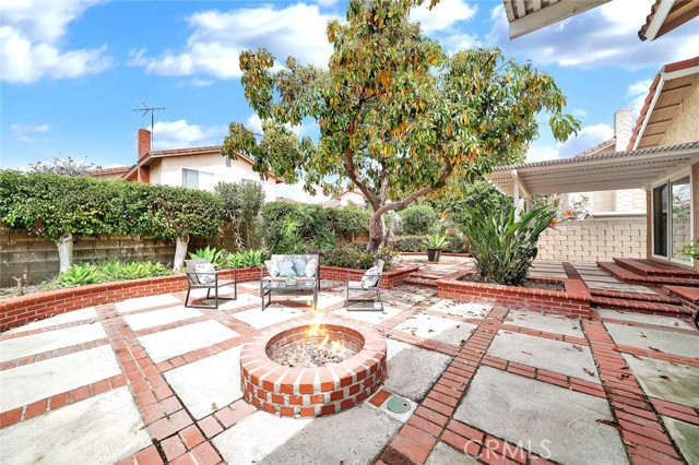 brick accented covered patios, fire pit, block wall surround, raised brick planters with lush landscaping and fruit trees