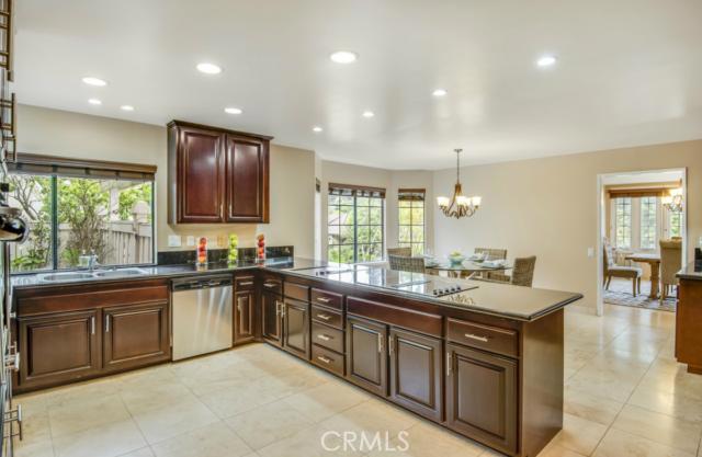 Large kitchen with granite counter top and bar seating. Travertine flooring, and recessed lighting. There are dark cherry cabinets and stainless appliances.