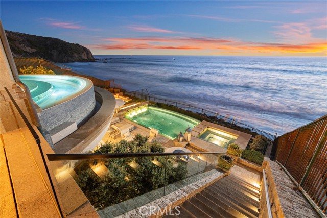 Settling for less isn’t an option at this absolutely stunning villa on the sand at The Strand at Headlands in Dana Point. Unobstructed front-row views span the azure Pacific Ocean, crashing waves, southern Orange County’s golden coastline, Catalina Island and the imposing headlands of historic Dana Point. Every level of the custom estate opens to the ocean, welcoming fresh sea breezes, natural light, and the hypnotic sounds of the surf into nearly every room. Extending approximately 10,576 square feet, the bespoke oceanfront mansion redefines elegance and sophistication with uncompromising craftsmanship and unyielding attention to detail. An appropriately grand entrance leads to a floating circular staircase that is crowned by a glass ceiling on the third level and provides a dramatic focal point on every floor. An elevator also serves each level of the home, which hosts five ensuite bedrooms and 7 full and 2 half baths. The formal foyer leads to a chic parlor, a formal dining room, and a massive great room with fireplace. Disappearing glass pocket doors open the great room to a large loggia that showcases a floating cantilevered spa with acrylic bottom that overlooks the beach. An island kitchen features a nook with built-in seating, and a separate catering kitchen and service bar. Take the stairs or elevator up to the top floor, where bedroom suites include a five-star owners retreat with sitting area, fireplace, ocean-view balcony, an oversized walk-in closet with island, and an exquisite bath. It’s all about fun and entertainment on the lowest floor, where a game room, billiards room, glass-enclosed wine cellar, service kitchen, fifth bedroom and a gym are located. This floor opens via a disappearing glass wall to a loggia with massive sunken wet bar. Beyond the bar awaits a resort pool and spa, a built-in island with grill, a seating area with open-air fireplace, extensive stone decking and direct beach access. Created by Homer Oatman of Oatman Architects, the estate was built by Mike Reeves of Corbin Reeves Construction and reveals exceptional interior design by Ohara Davies-Gaetano. Sequestered behind guarded gates, The Strand at Headlands is one of the most coveted oceanfront communities in California and offers more than one mile of coastline, 70 acres of parks, scenic trails, a beach club and easy access to resorts, shops, restaurants and outstanding schools.