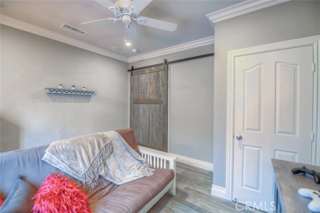 Downstairs bedroom currently being used as a den/media room with barn door, closet, crown molding, ceiling fan, plantation shutters, wood-like tile flooring, recessed lighting, speakers, and wired for wall mounted TVs.